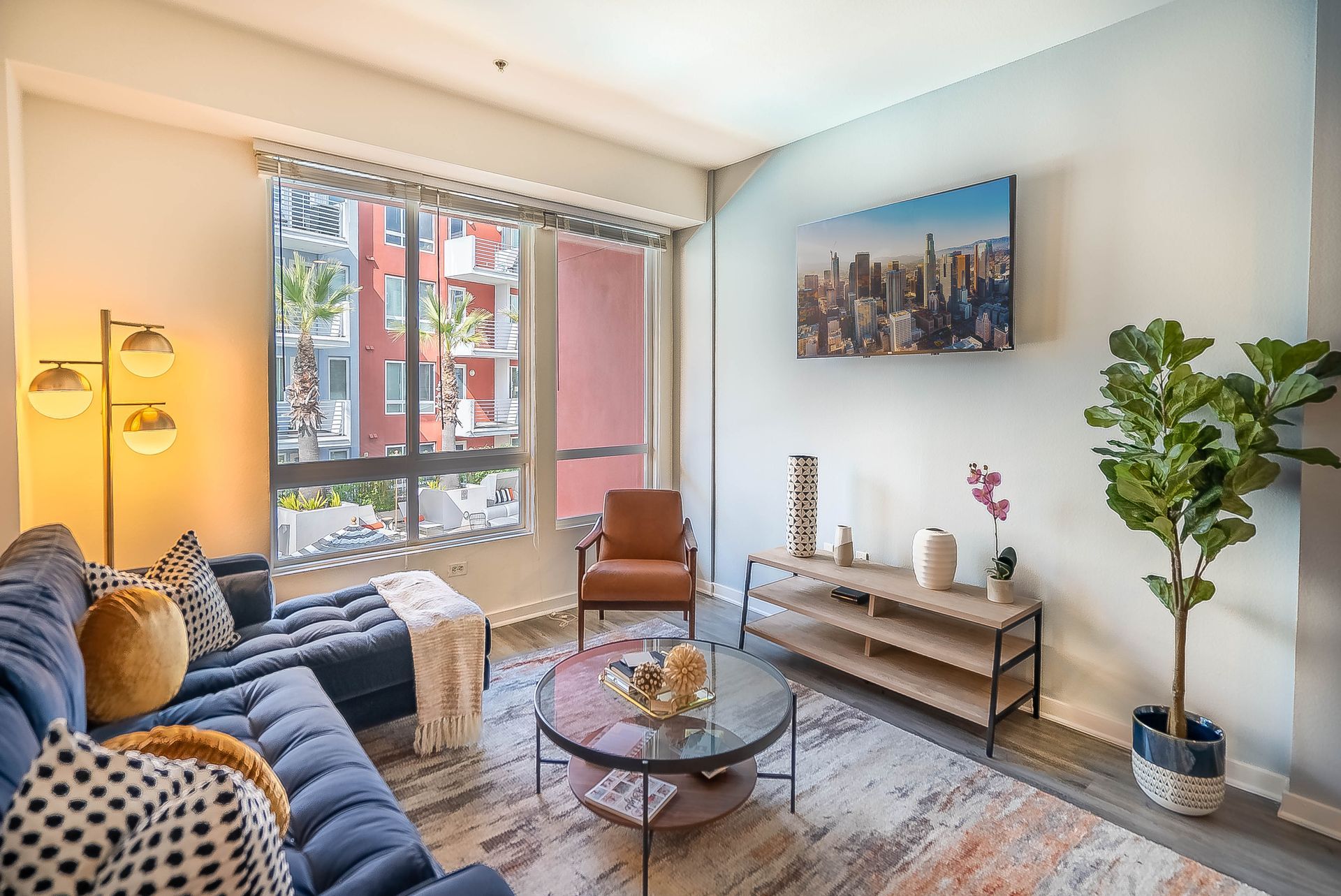 A living room with a blue couch , coffee table , chairs and a painting on the wall.