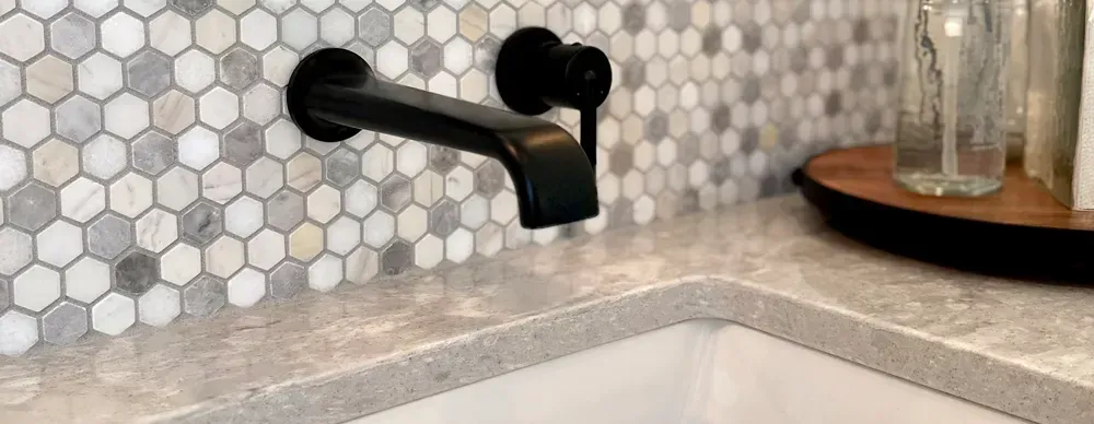 A bathroom sink with a black faucet and hexagon tiles on the wall.