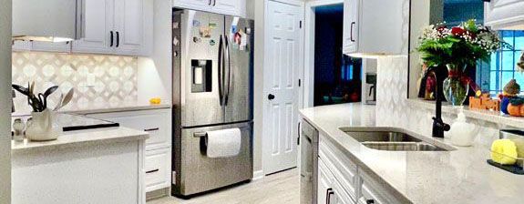 A kitchen with white cabinets , a stainless steel refrigerator , a sink , and a window.