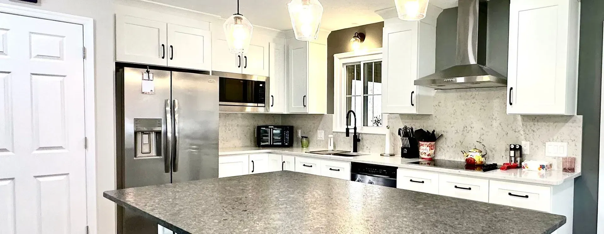 A kitchen with white cabinets , granite counter tops , stainless steel appliances and a large island.