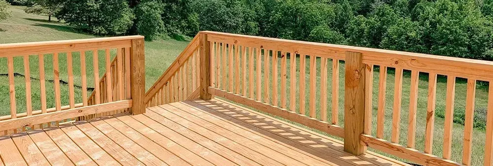 A wooden deck with a wooden railing surrounded by trees and grass.