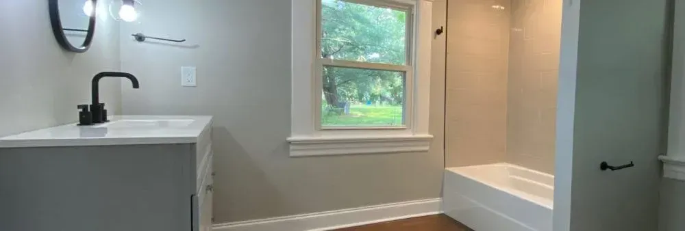 A bathroom with a sink , toilet , shower and window.