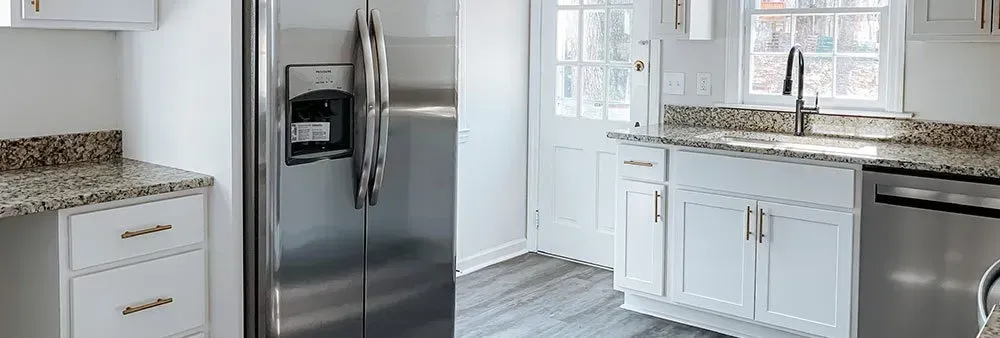 A kitchen with stainless steel appliances , white cabinets , granite counter tops and a refrigerator.