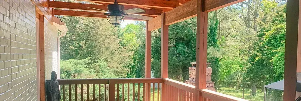 A screened in porch with a ceiling fan and a view of trees.