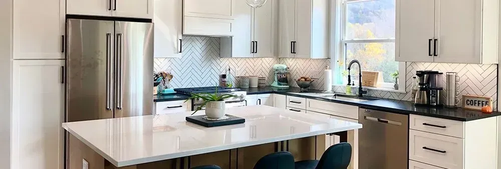 A kitchen with white cabinets , black counter tops , stainless steel appliances and a large island.