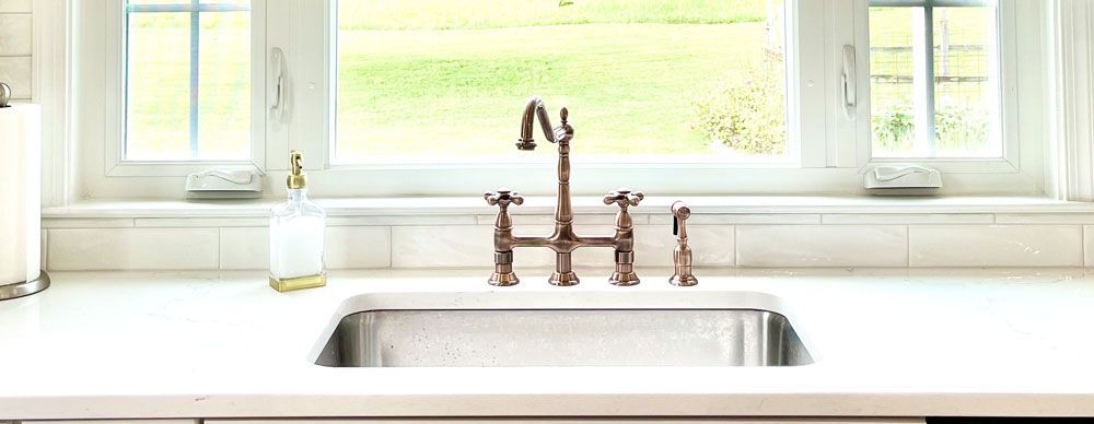 A kitchen sink with a faucet and a window in the background.