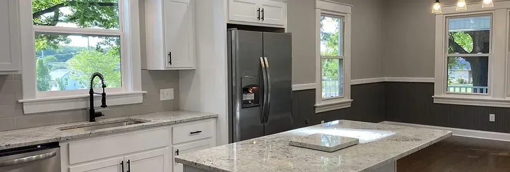 A kitchen with white cabinets , granite counter tops , stainless steel appliances and a refrigerator.