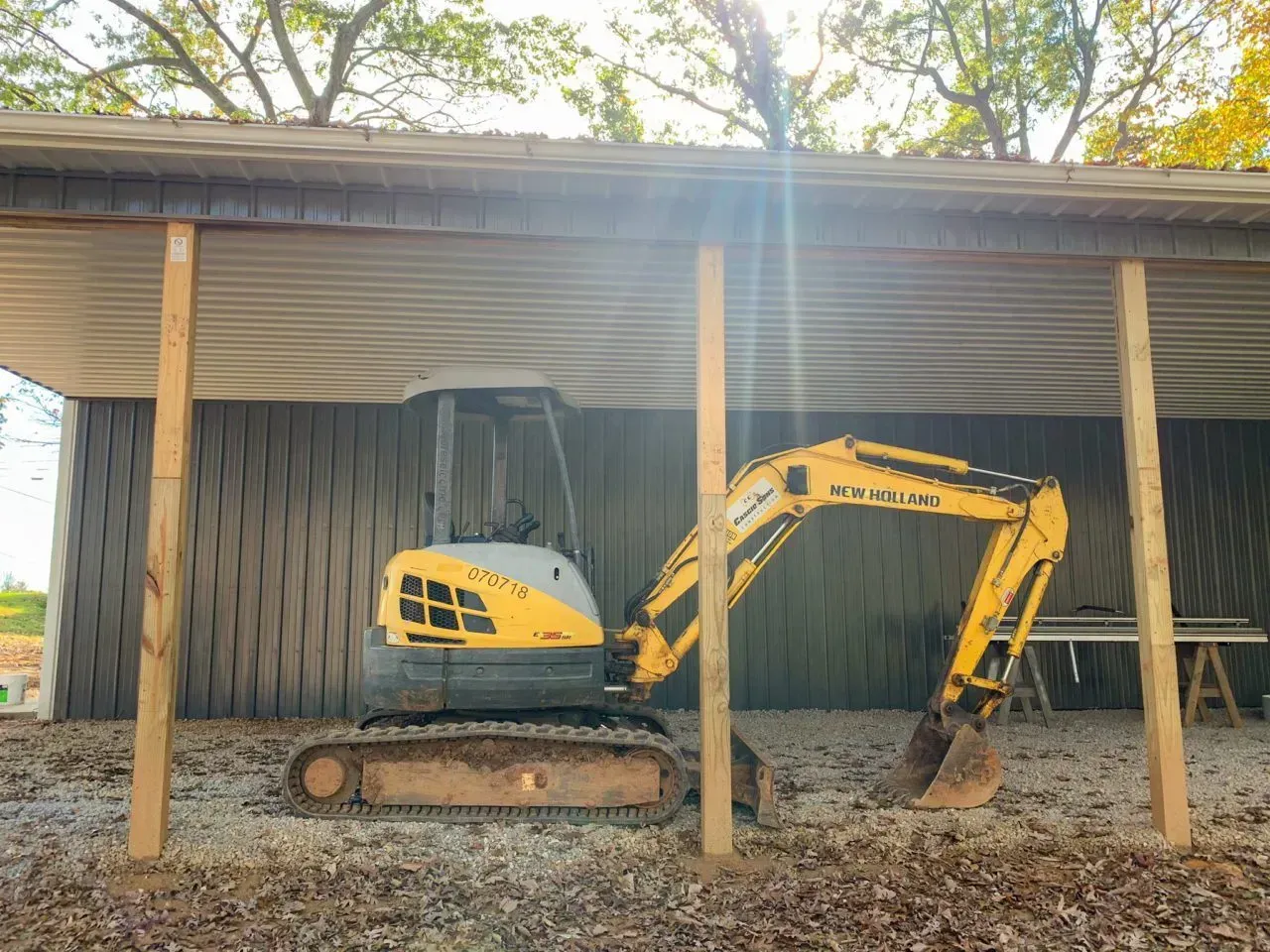 A small yellow excavator is parked under a covered area.