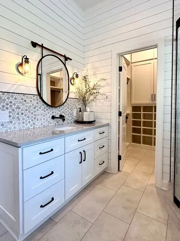 A bathroom with white cabinets , a sink , a mirror and a walk in shower.