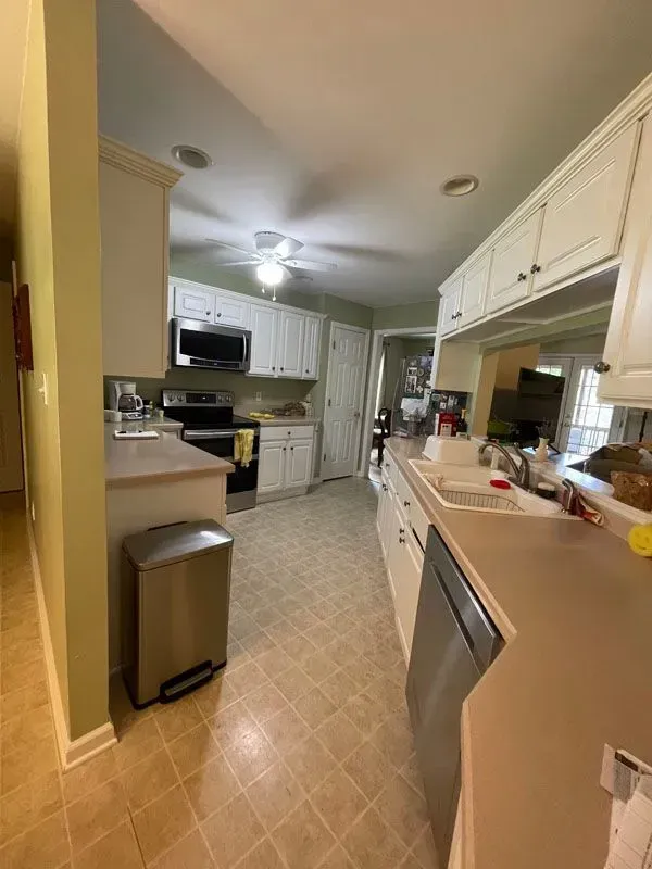 A kitchen with white cabinets , stainless steel appliances , and a trash can.