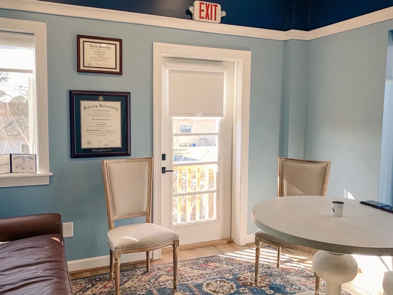 A room with blue walls , white chairs , a table and an exit sign.