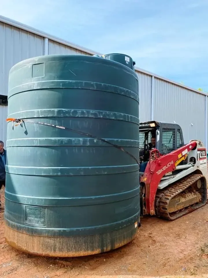 A large green tank is sitting next to a bulldozer in front of a building.