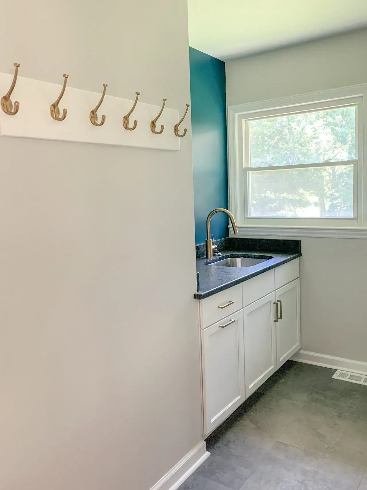 A laundry room with a sink , cabinets and hooks on the wall.