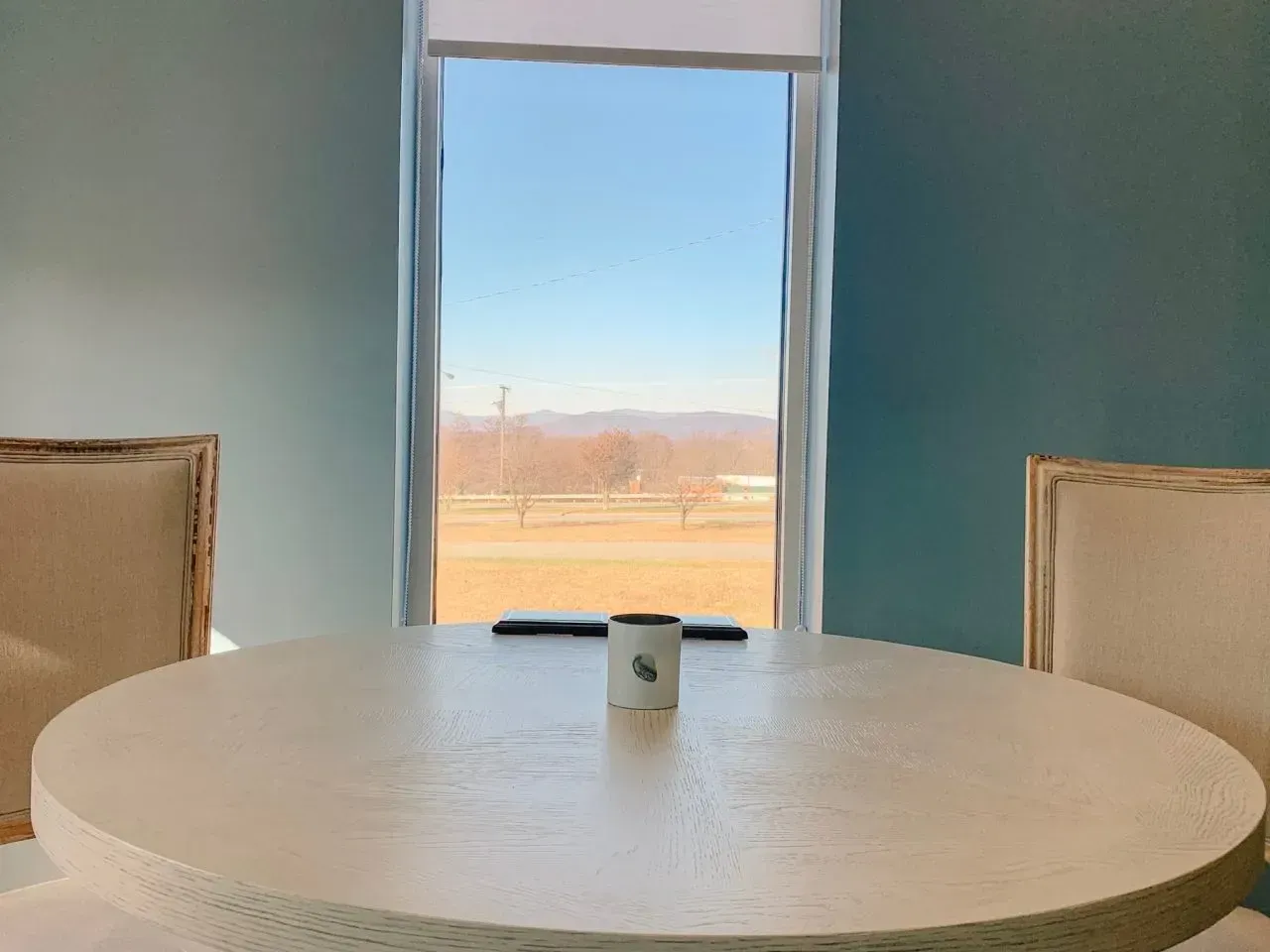 A round table with a cup on it in front of a window.