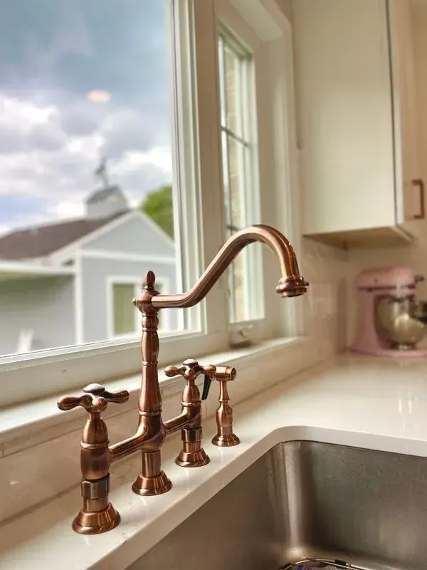 A kitchen sink with a copper faucet next to a window.