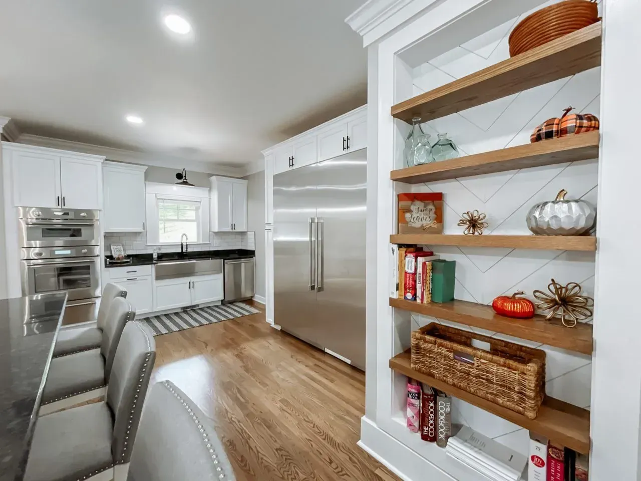 A kitchen with white cabinets and stainless steel appliances and wooden shelves.