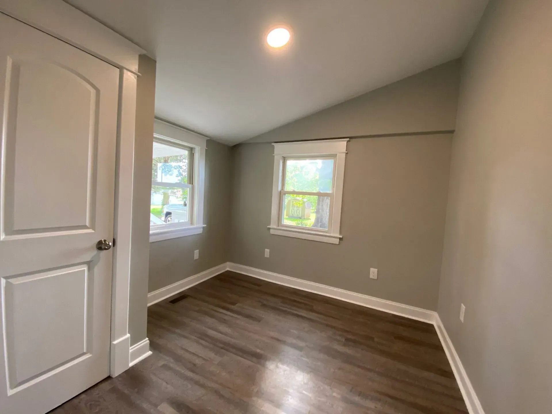 An empty room with hardwood floors and two windows.
