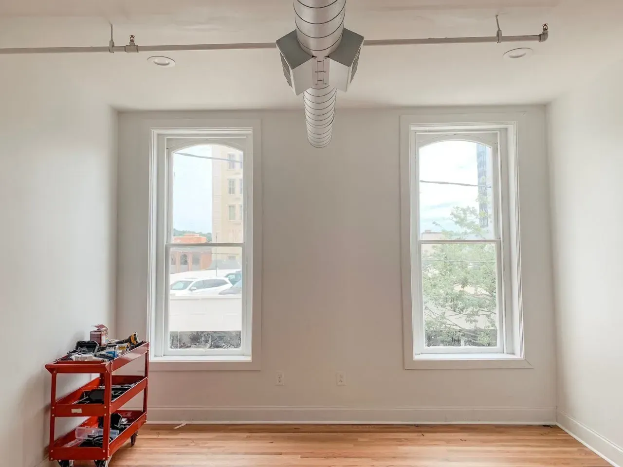 An empty room with two windows and a red cart on the floor.