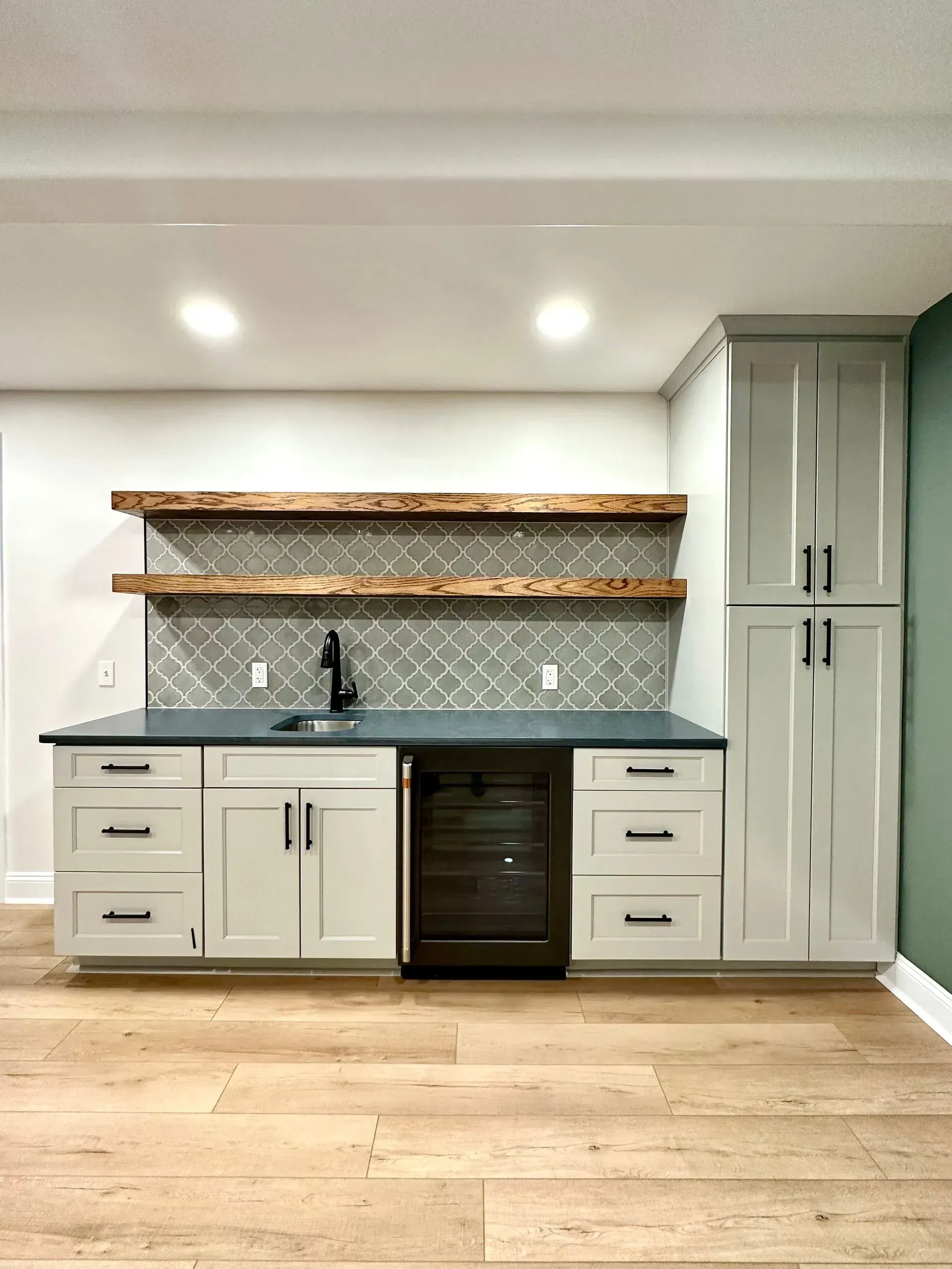 A kitchen with white cabinets , a sink , and a wine cooler.