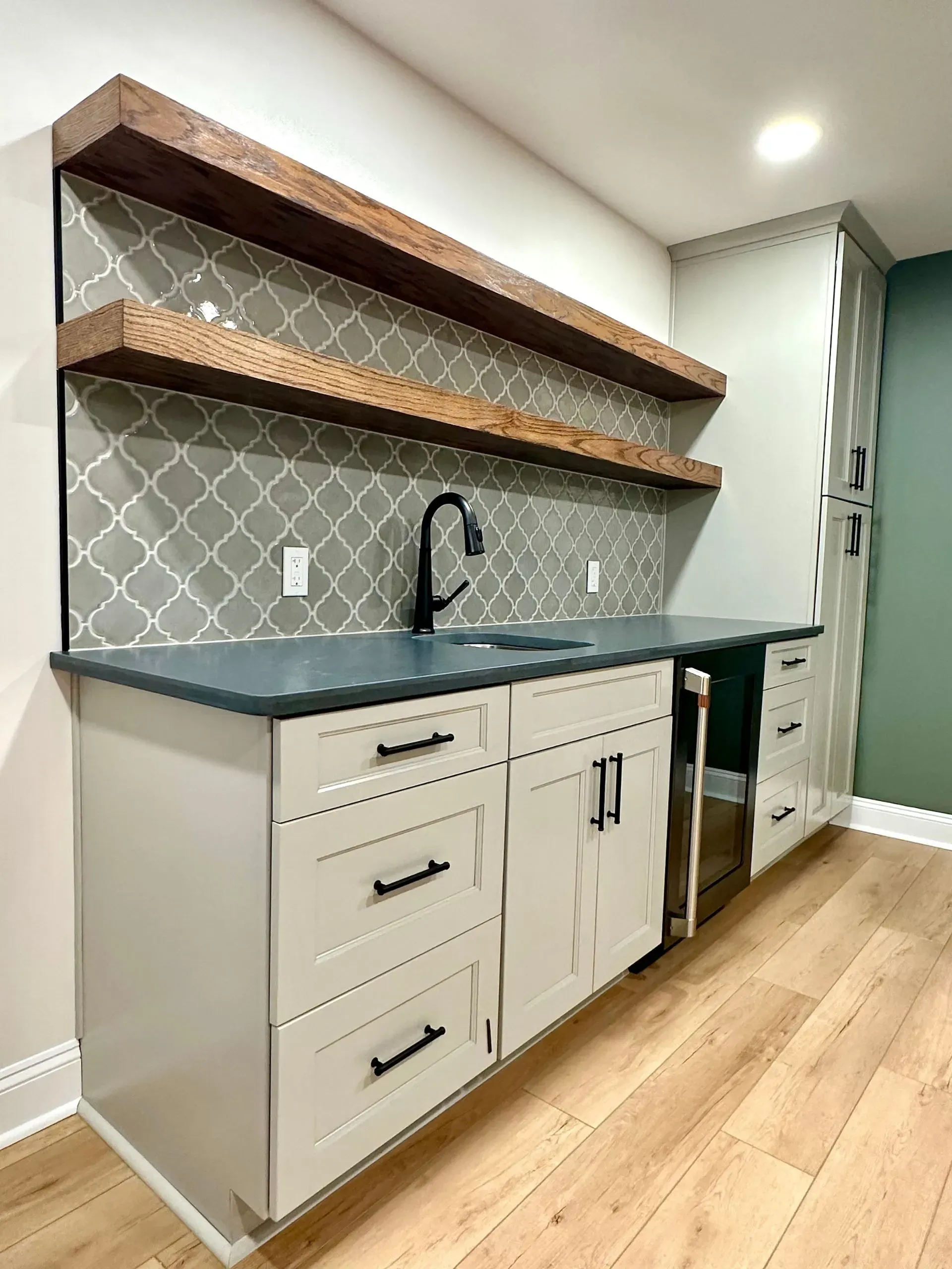 A kitchen with white cabinets , black counter tops , and wooden floors.