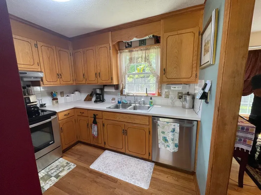 A kitchen with wooden cabinets , stainless steel appliances , a sink , and a window.