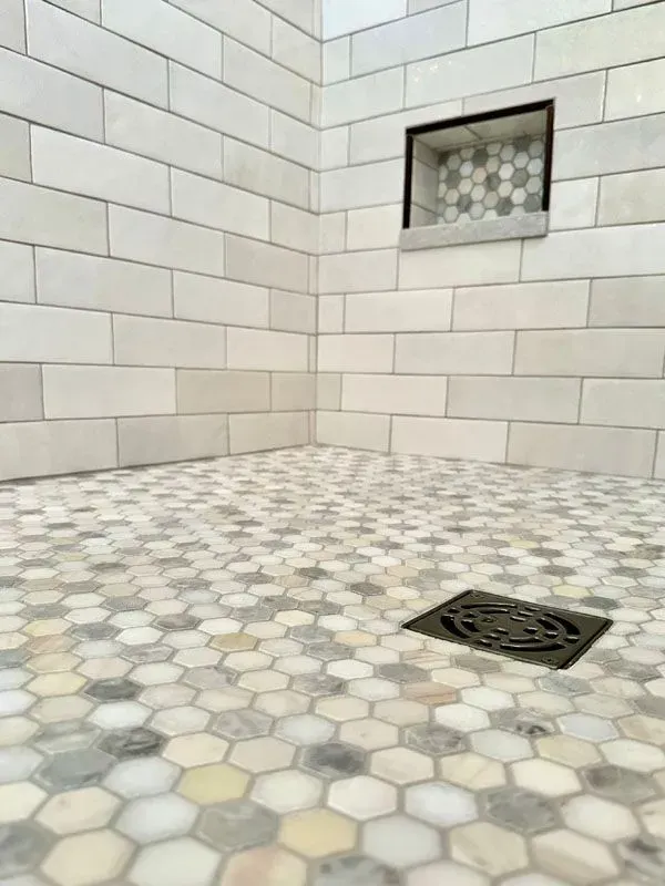 A shower with a hexagonal tile floor and a drain.