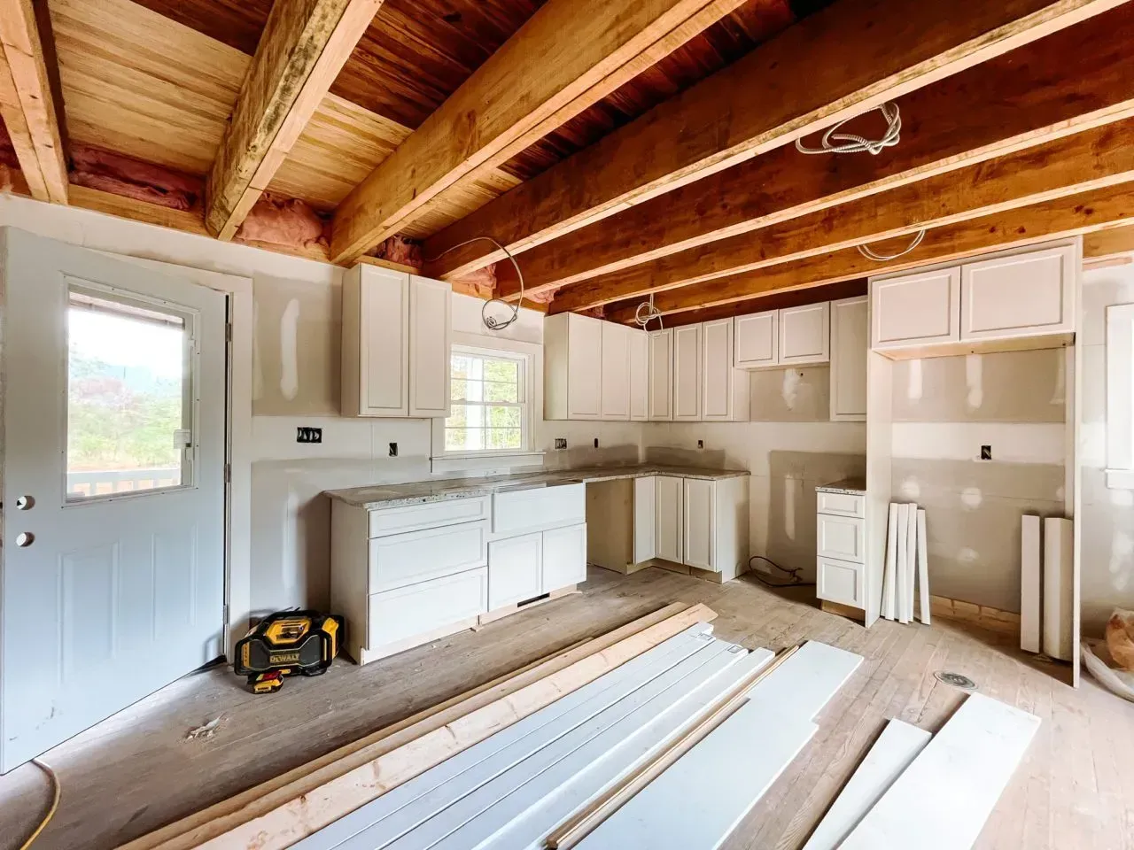A kitchen under construction with white cabinets and wooden beams.