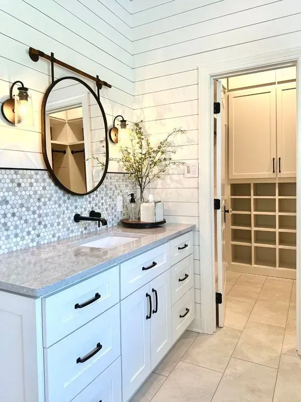A bathroom with white cabinets , a sink , a mirror and a walk in closet.