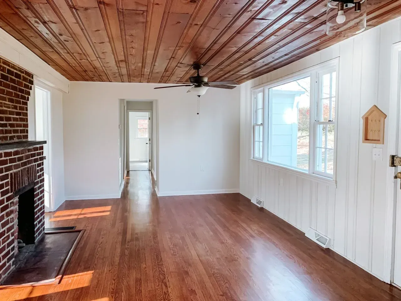 An empty living room with hardwood floors a fireplace and a ceiling fan.