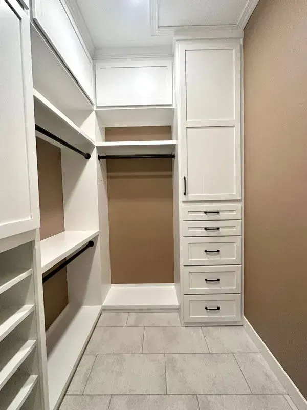 A walk in closet with white cabinets and drawers.