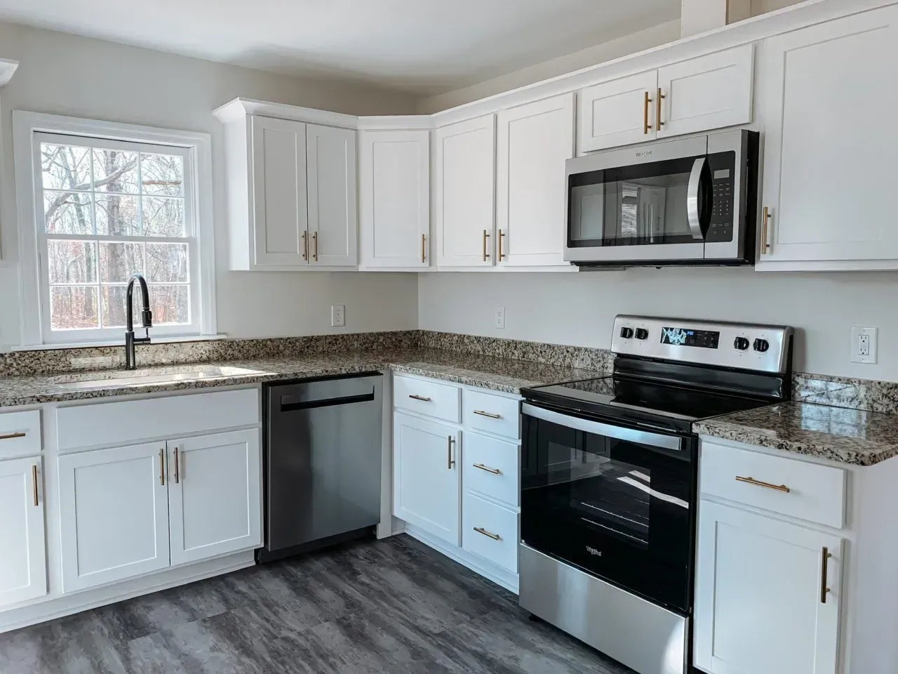 A kitchen with white cabinets , stainless steel appliances , granite counter tops and a window.