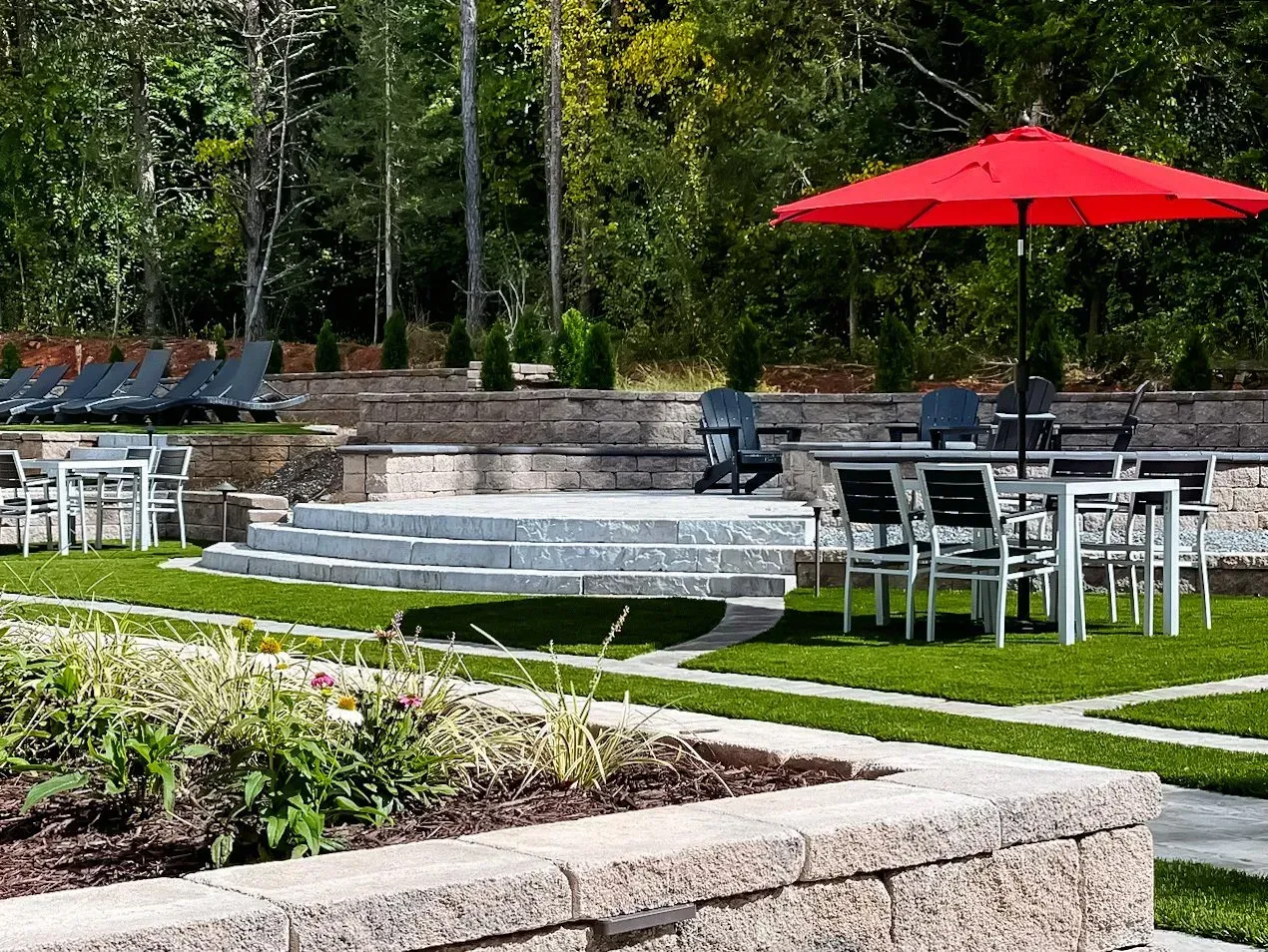 A patio with tables and chairs and a red umbrella.