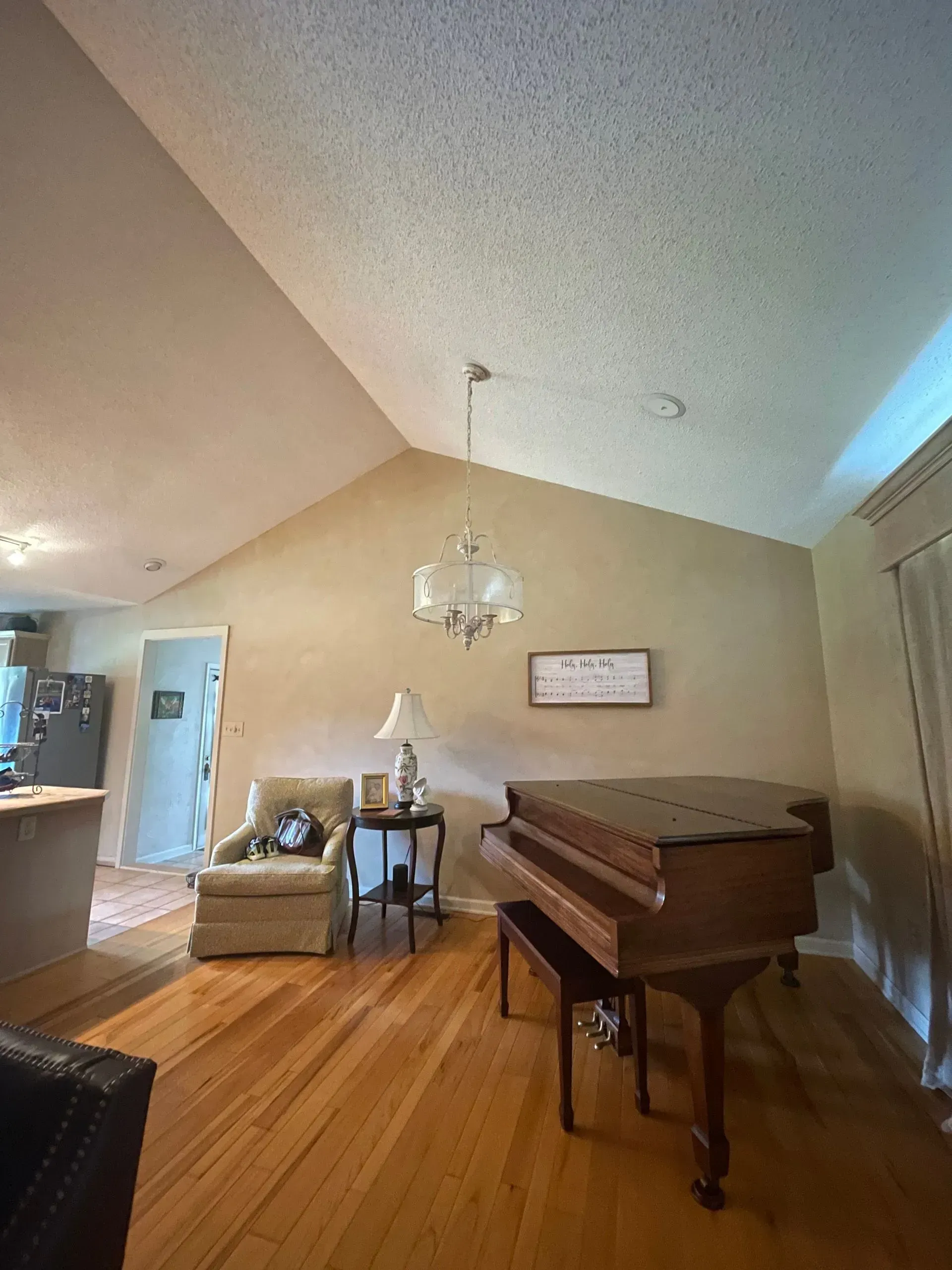 A living room with a piano , chair , table and chandelier.