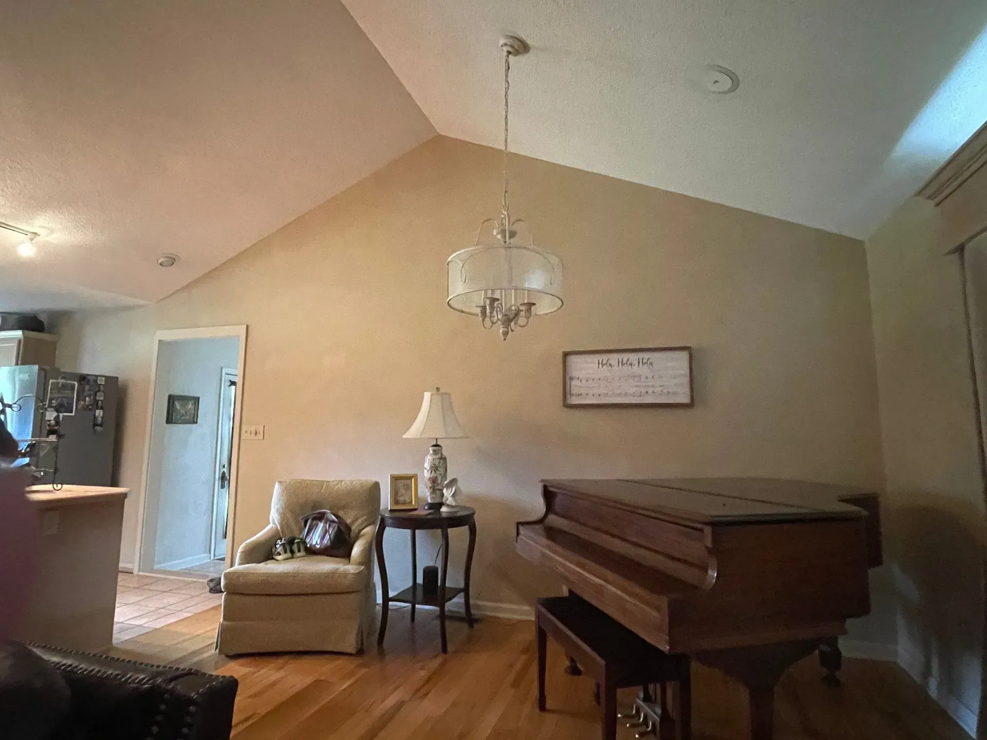 A living room with a piano , chair , lamp and chandelier.