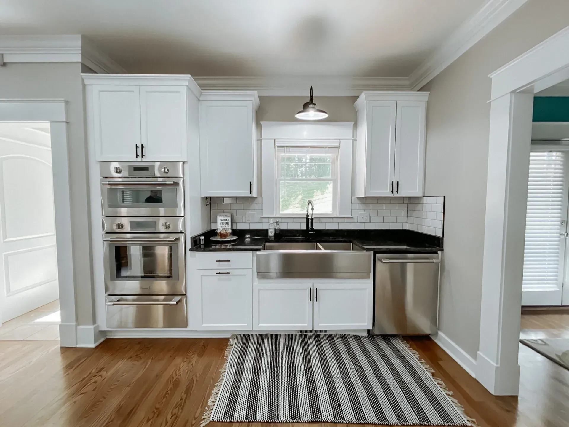 A kitchen with white cabinets , stainless steel appliances , a sink , and a rug.