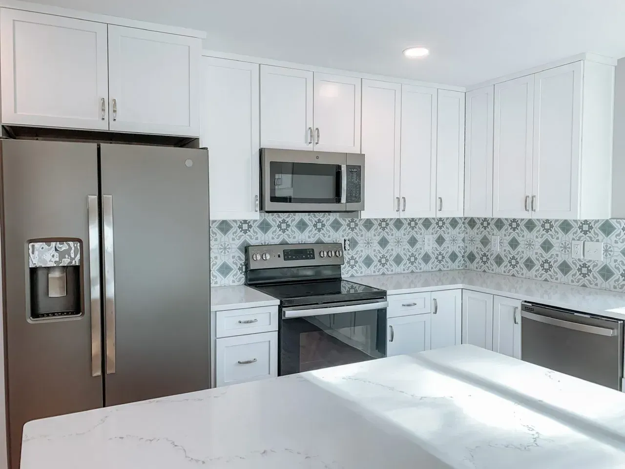 A kitchen with white cabinets , a black refrigerator , a stove , and a microwave.