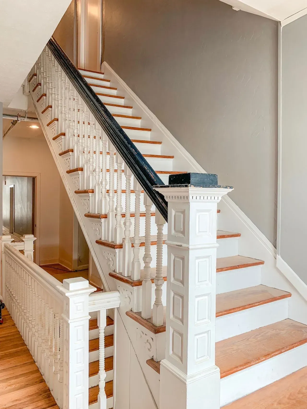 A white staircase with wooden steps and a black railing in a house.