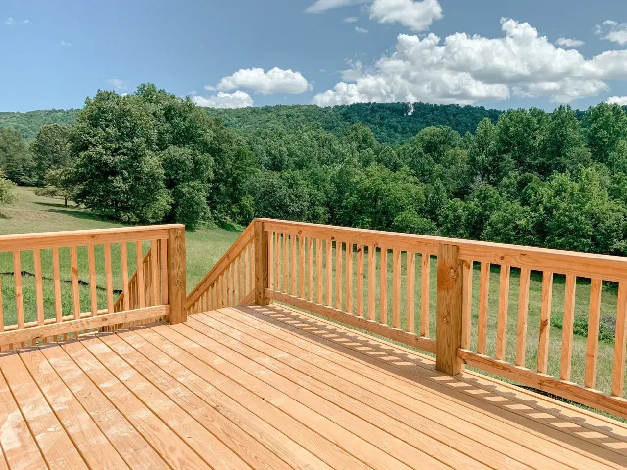 A wooden deck with a railing overlooking a field and trees.