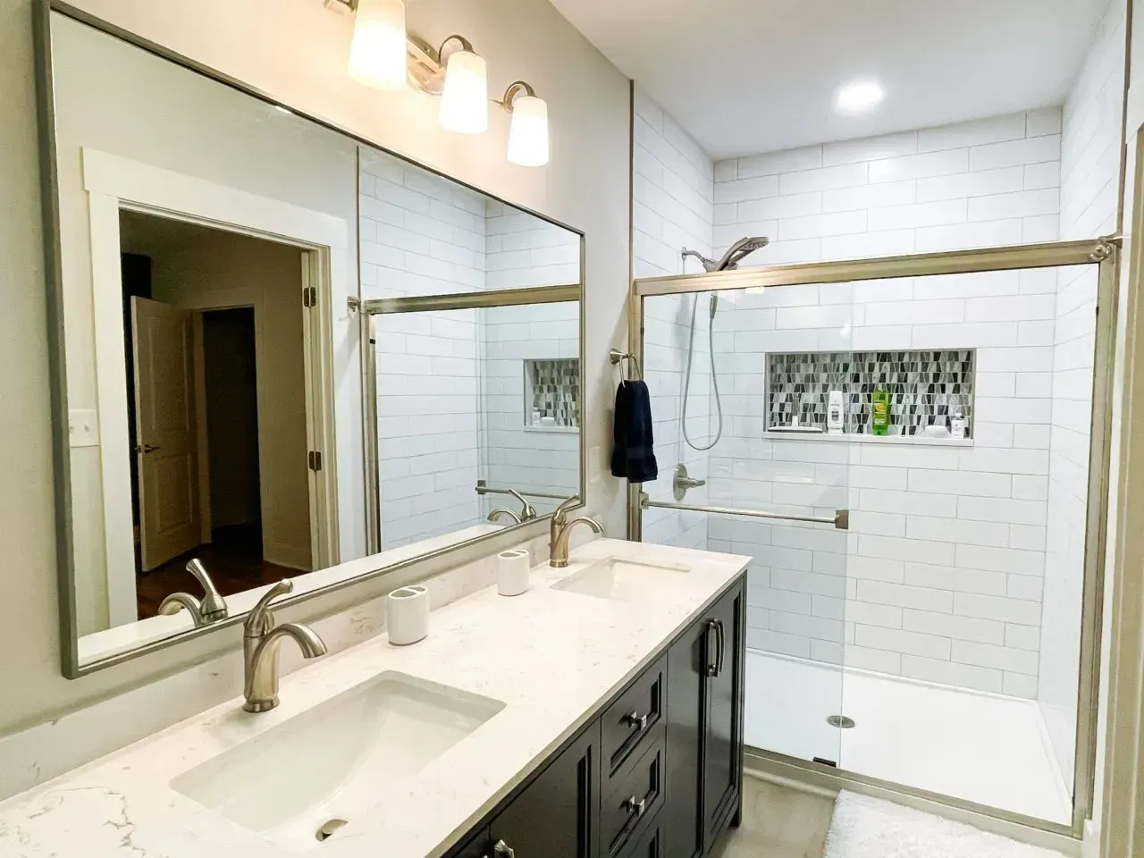 A bathroom with two sinks , a shower , and a large mirror.