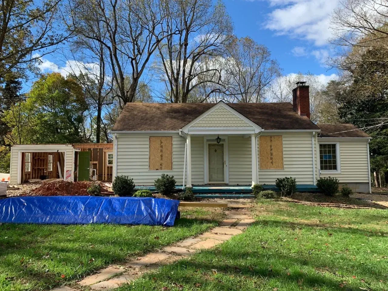 A white house with a blue tarp in front of it is being remodeled.