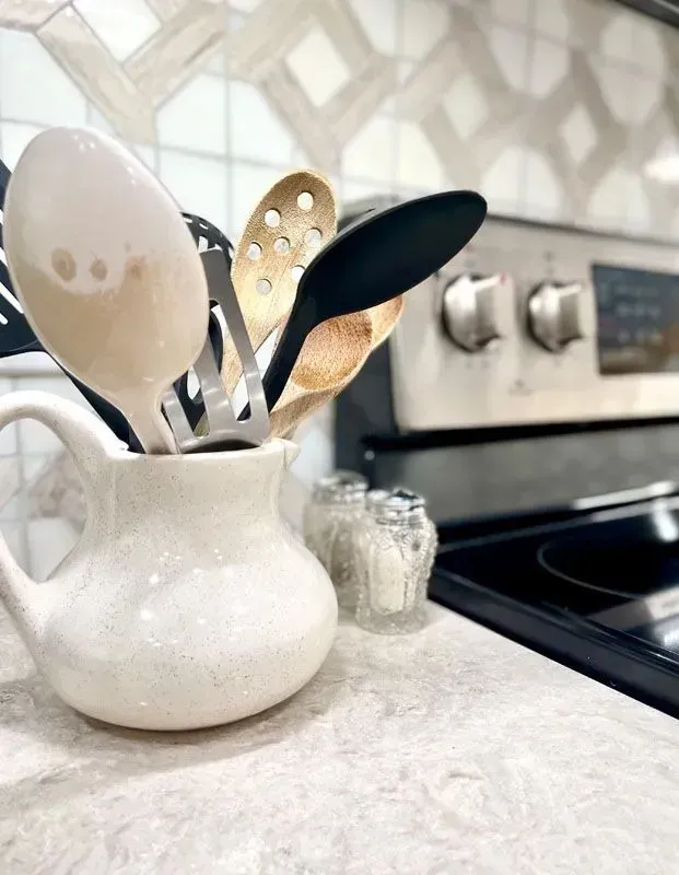 A white pitcher filled with kitchen utensils sits on a counter in front of a stove