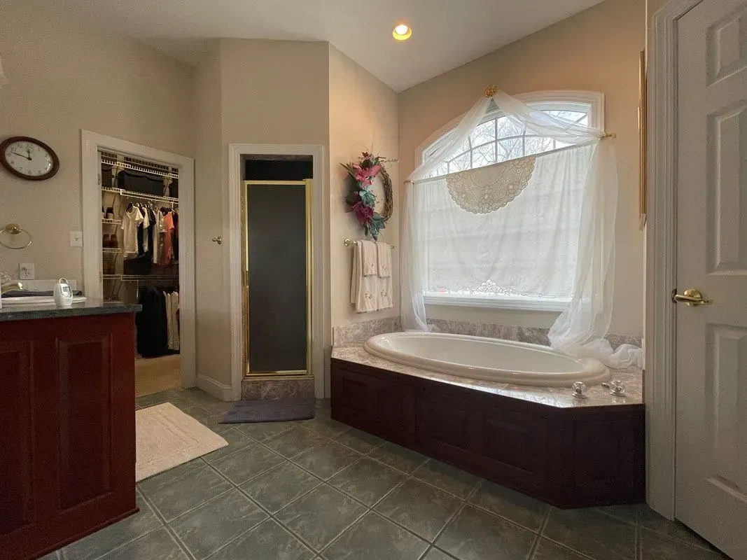 A bathroom with a tub , sink , and window.
