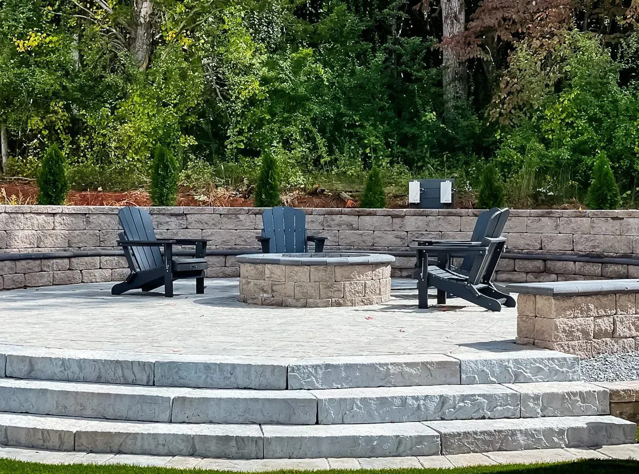 There is a fire pit in the middle of the patio with chairs around it.