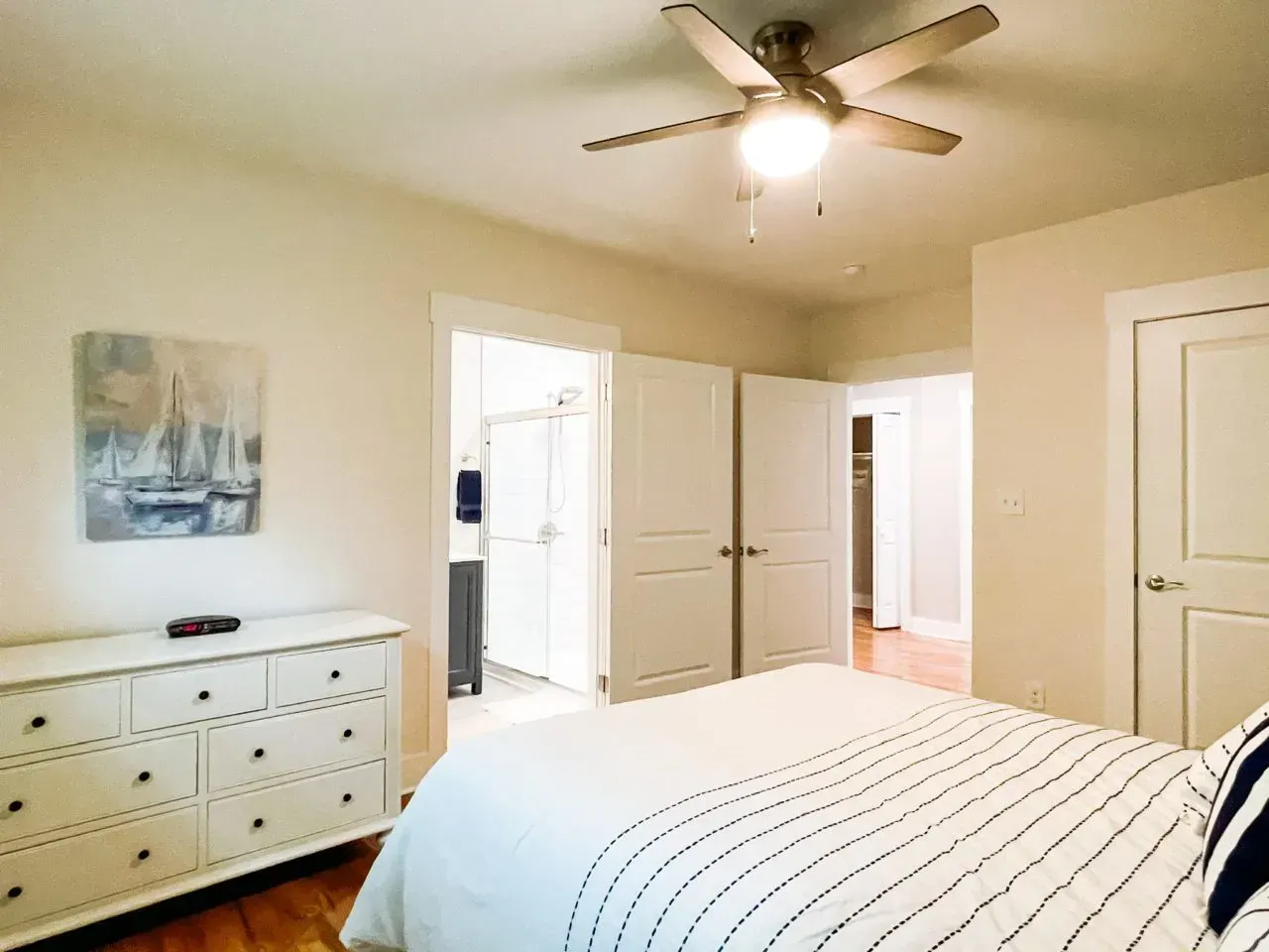 A bedroom with a bed , dresser , and ceiling fan.