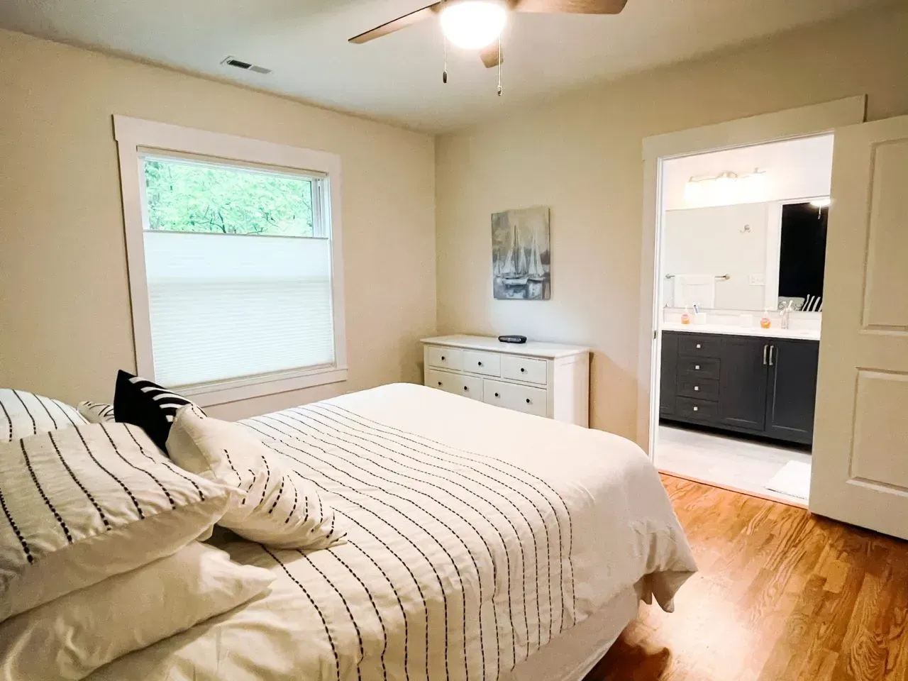 A bedroom with a bed , dresser , window and ceiling fan.