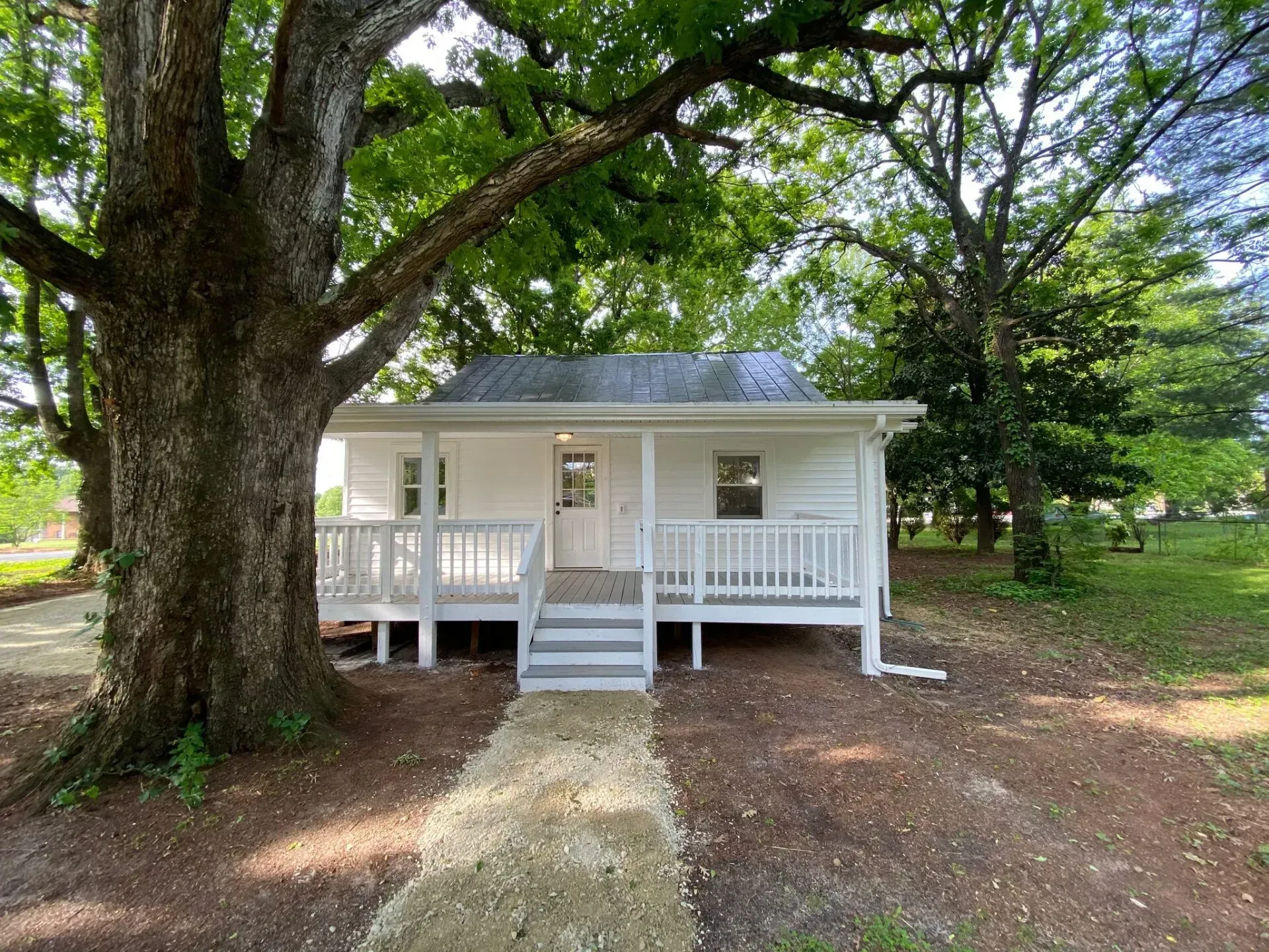 A small white house with a porch and stairs is surrounded by trees.
