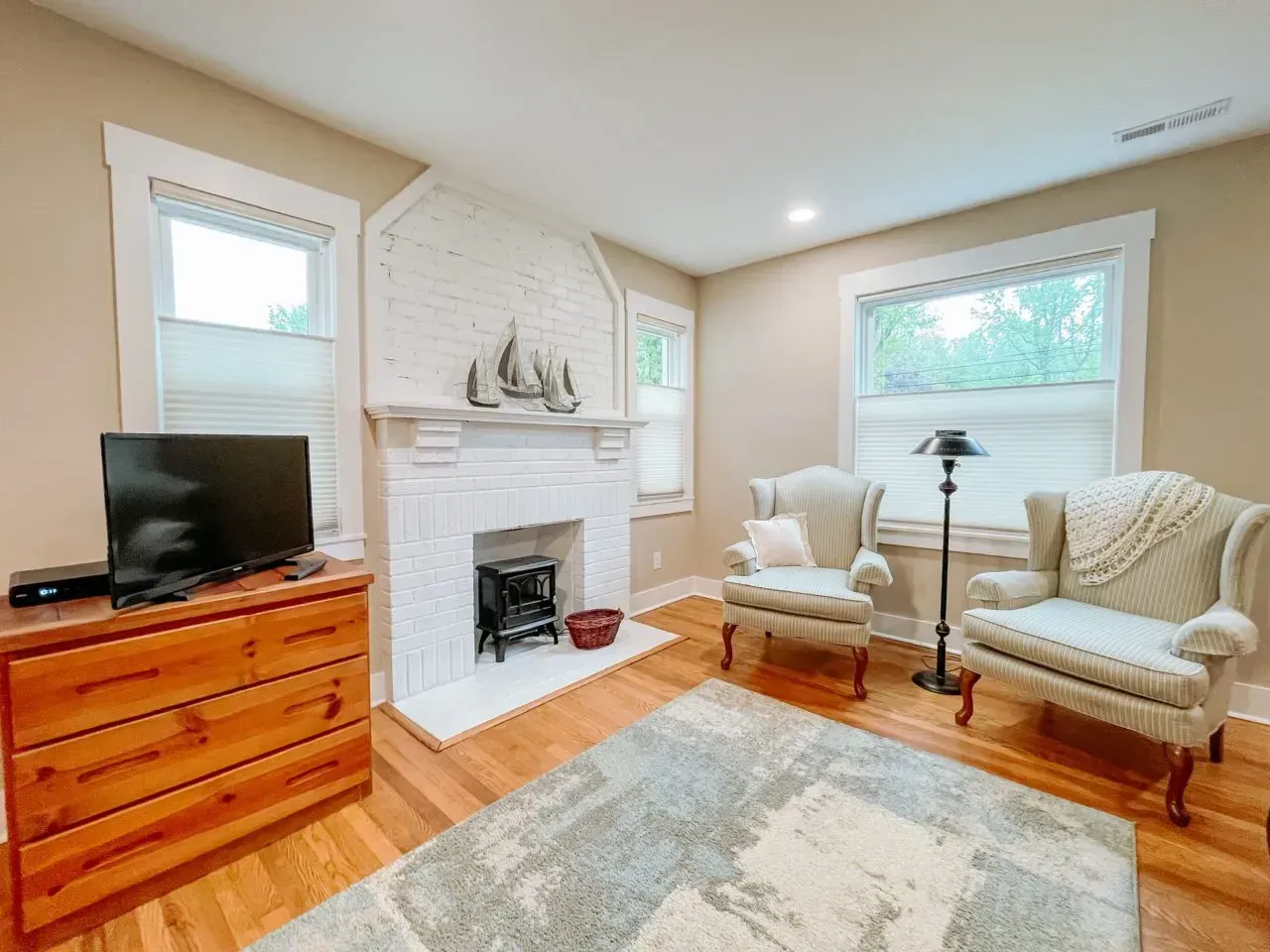 A living room with a fireplace , chairs , a dresser and a flat screen tv.