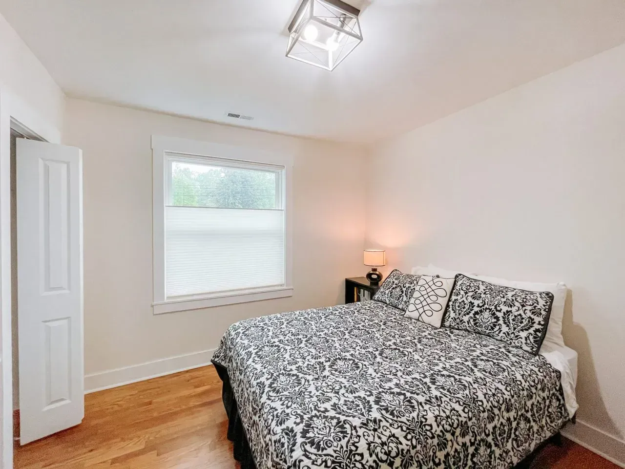 A bedroom with a bed , window and hardwood floors.