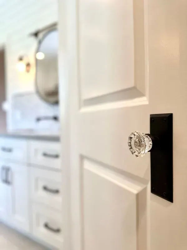 A white door with a clear glass door knob in a bathroom.