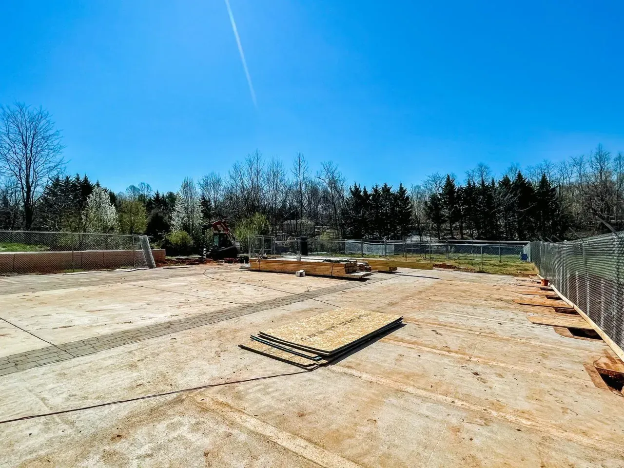 A large empty construction site with a fence and trees in the background.